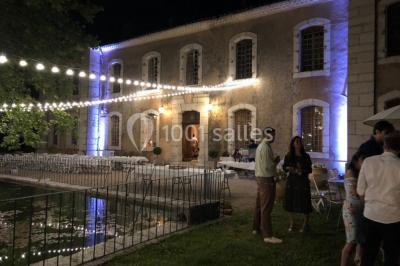 Vue sur un lac entouré de collines verdoyantes à travers une fenêtre ouverte avec des volets en bois.