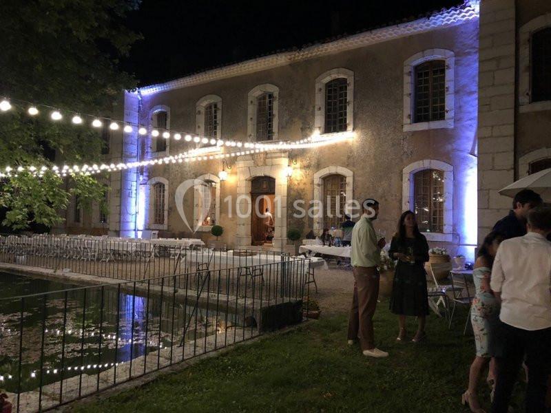 Façade éclairée d'un bâtiment ancien la nuit, avec des guirlandes lumineuses et des invités discutant en extérieur.