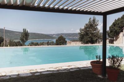 Vue sur un lac entouré de collines verdoyantes à travers une fenêtre ouverte avec des volets en bois.