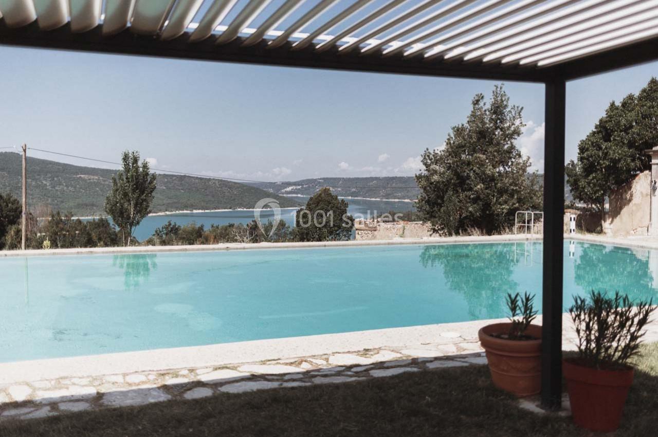 Vue d'une piscine extérieure avec un toit à lames, donnant sur un paysage de lac et de collines verdoyantes.