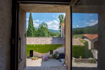Vue sur un lac entouré de collines verdoyantes à travers une fenêtre ouverte avec des volets en bois.