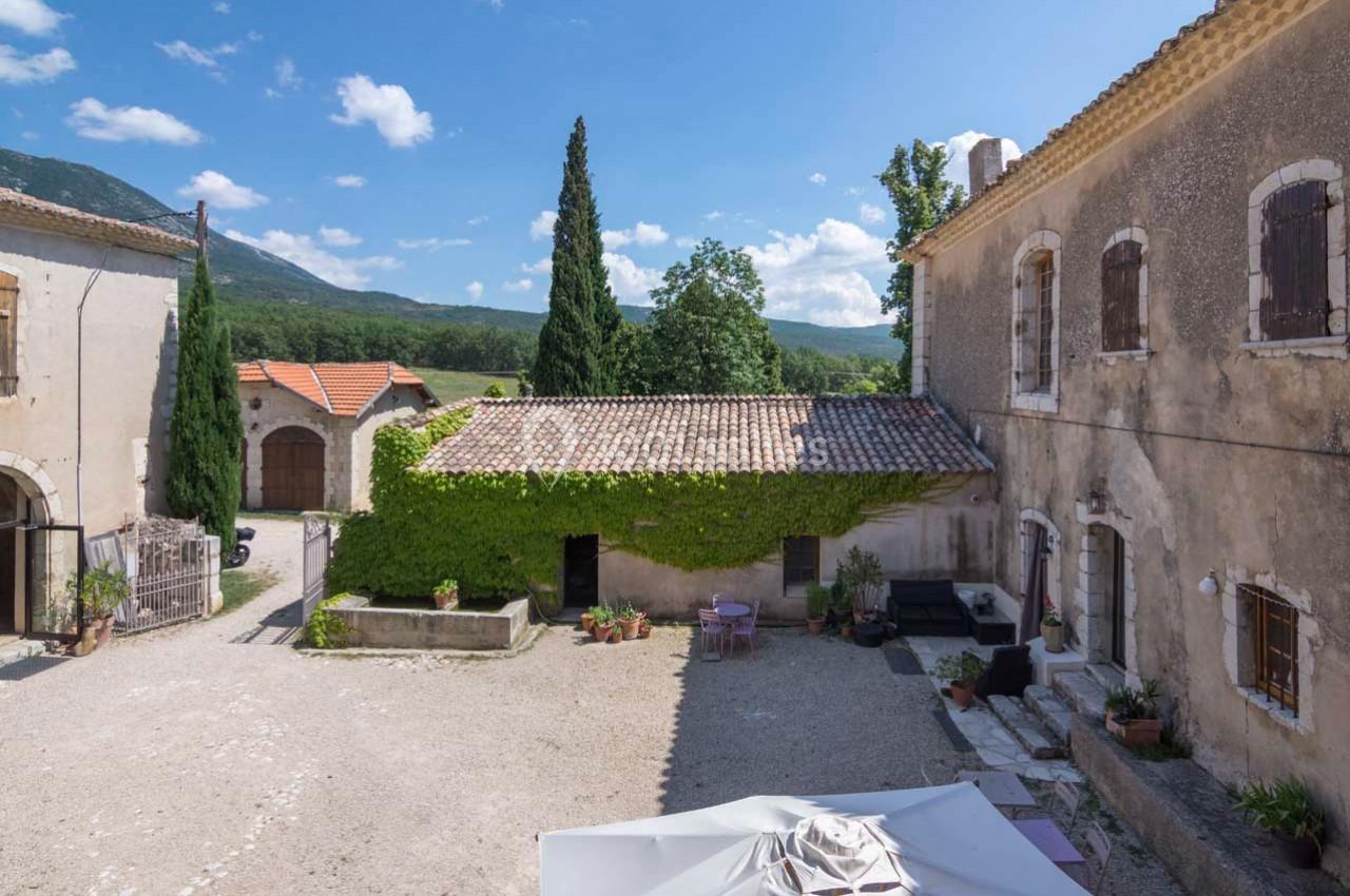 Cour d'une maison en pierre avec murs recouverts de lierre, entourée de bâtiments anciens et vue sur des collines…