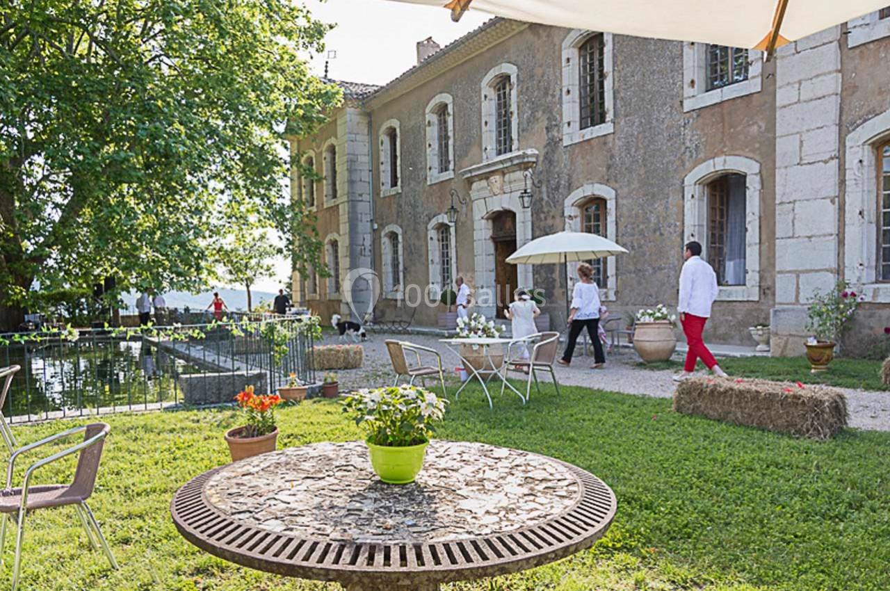 Terrasse d'un domaine ancien avec des tables, des chaises et des visiteurs près d'un bassin entouré de verdure.