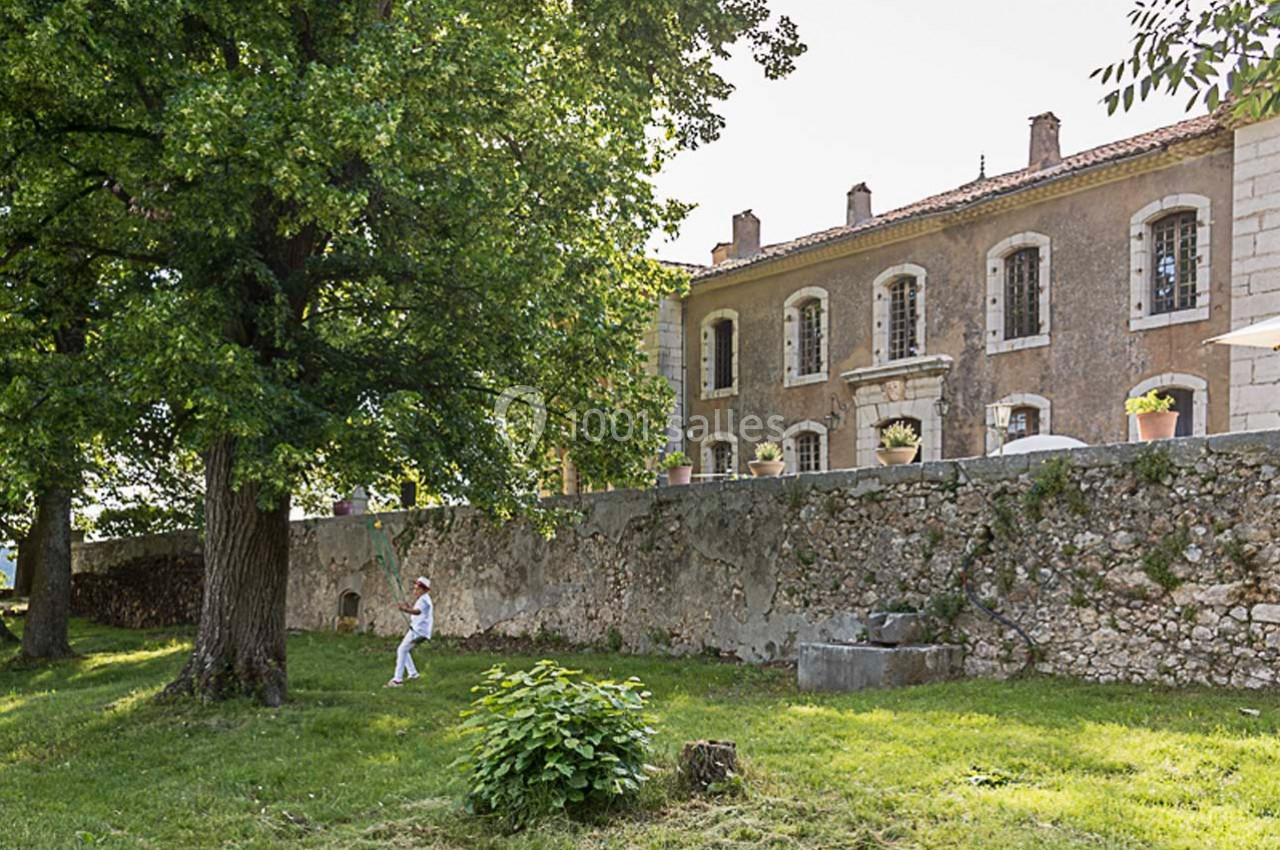 Façade d'un bâtiment en pierre avec des volets, vue depuis un jardin arboré sous un ciel clair.