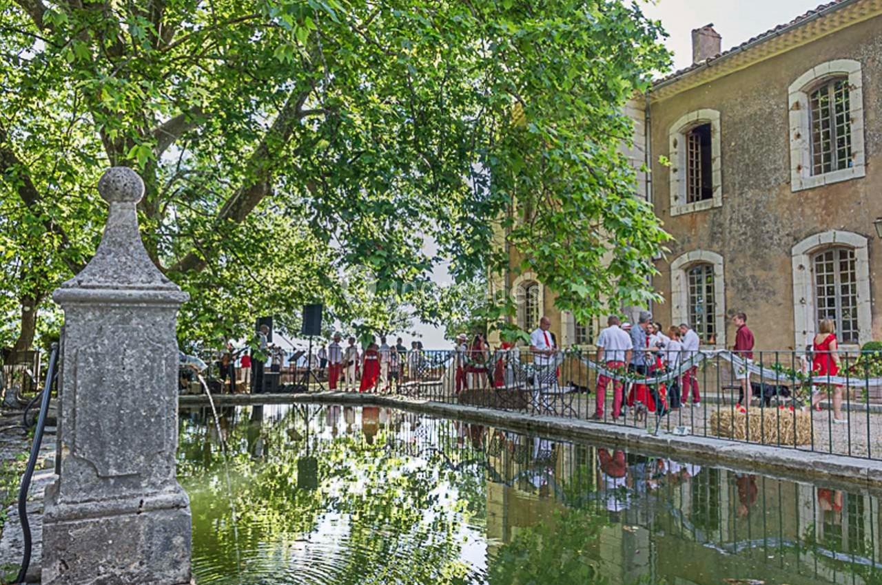 Un groupe de personnes en tenue traditionnelle se rassemble près d'un bassin entouré d'arbres et d'un bâtiment ancien.