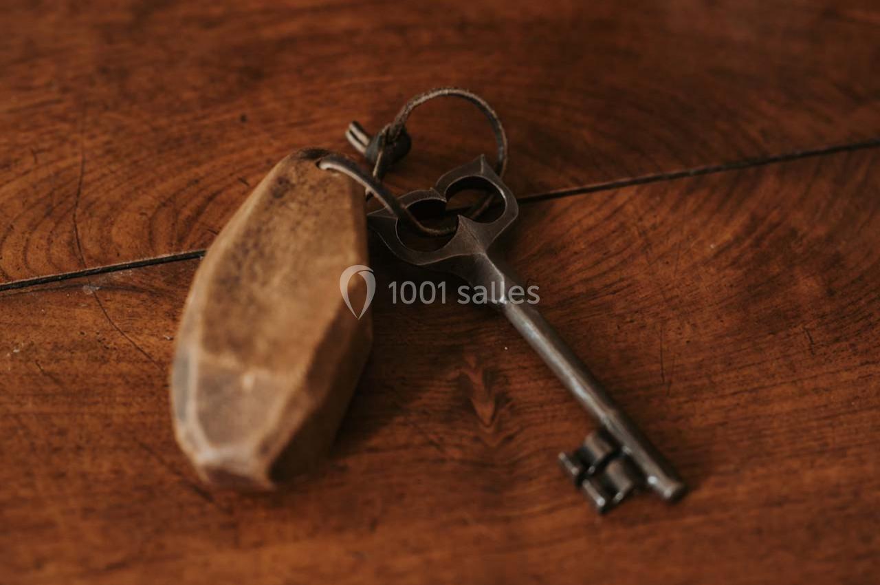 Clé ancienne en métal avec un porte-clés en bois posé sur une surface en bois.