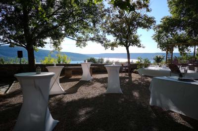 Vue sur un lac entouré de collines verdoyantes à travers une fenêtre ouverte avec des volets en bois.
