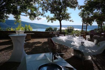 Vue sur un lac entouré de collines verdoyantes à travers une fenêtre ouverte avec des volets en bois.