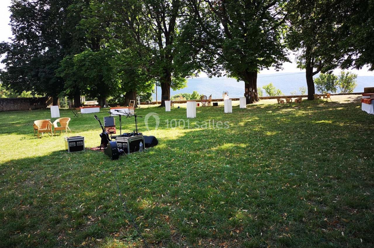 Pelouse ombragée avec équipements audio et mobilier dispersé, vue sur un plan d'eau en arrière-plan.