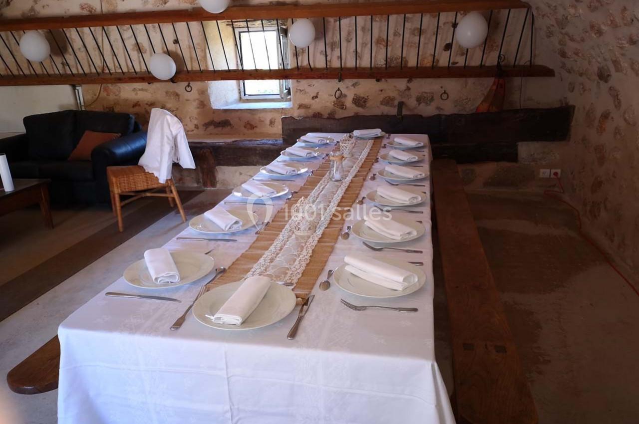 Table en bois dressée avec une nappe blanche, des assiettes, des serviettes pliées et des couverts, dans une salle rustique.