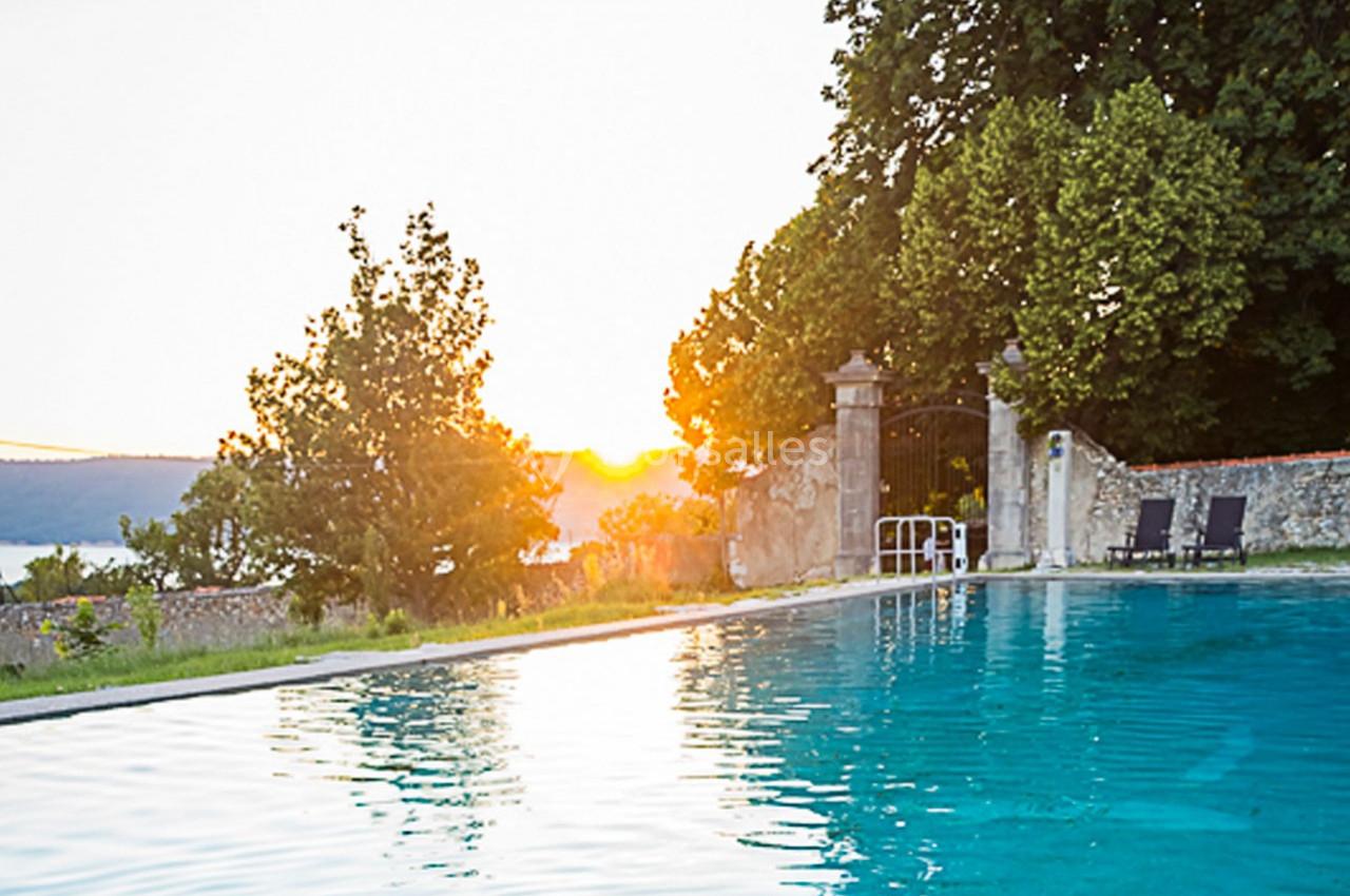 Piscine extérieure entourée de verdure, avec un coucher de soleil et un portail en arrière-plan.