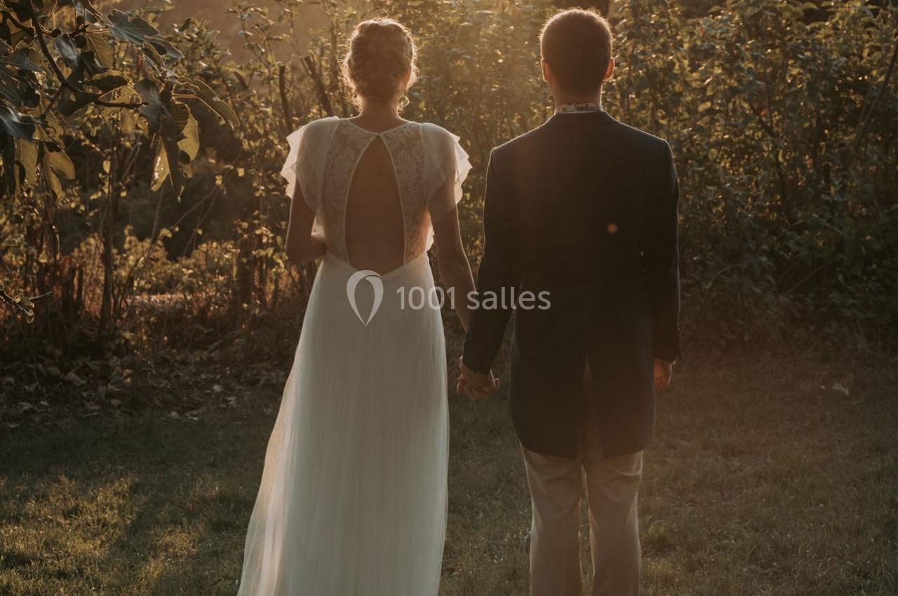 Un couple de dos, tenant la main, vêtu élégamment, dans un jardin au coucher du soleil.