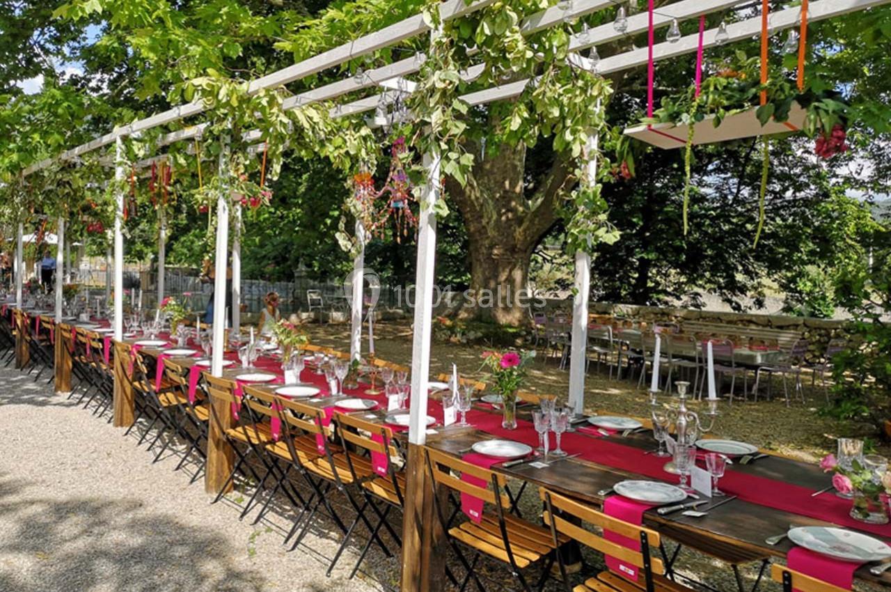 Tables longues décorées pour un repas en plein air, sous une pergola ornée de feuillage et de fleurs colorées.