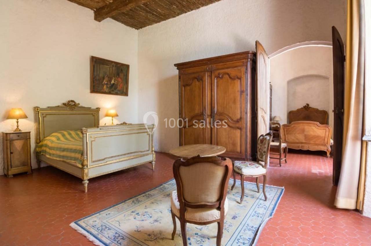 Chambre rustique avec lit ancien, armoire en bois, chaises classiques, tapis clair et sol en tomettes rouges.