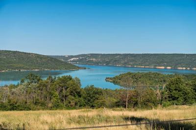 Vue sur un lac entouré de collines verdoyantes à travers une fenêtre ouverte avec des volets en bois.
