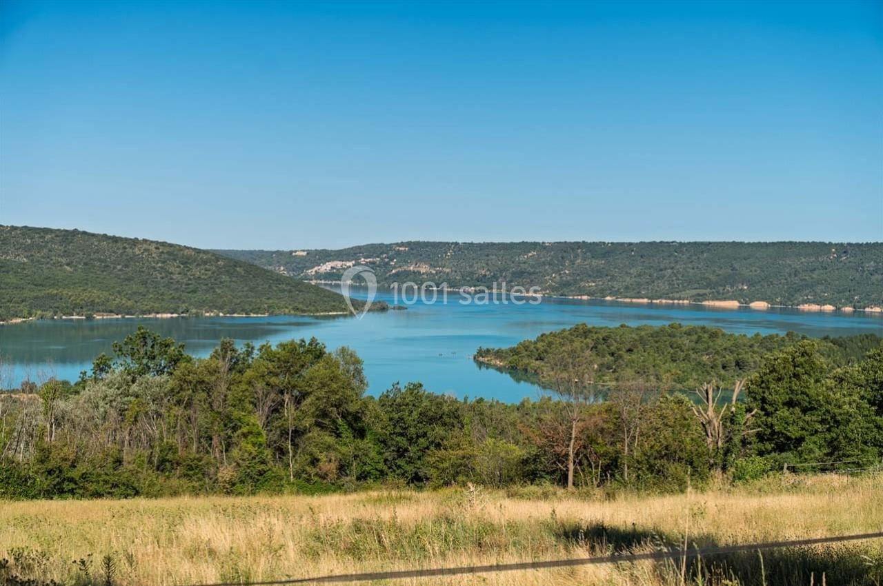 Paysage avec un lac entouré de collines verdoyantes sous un ciel bleu clair.