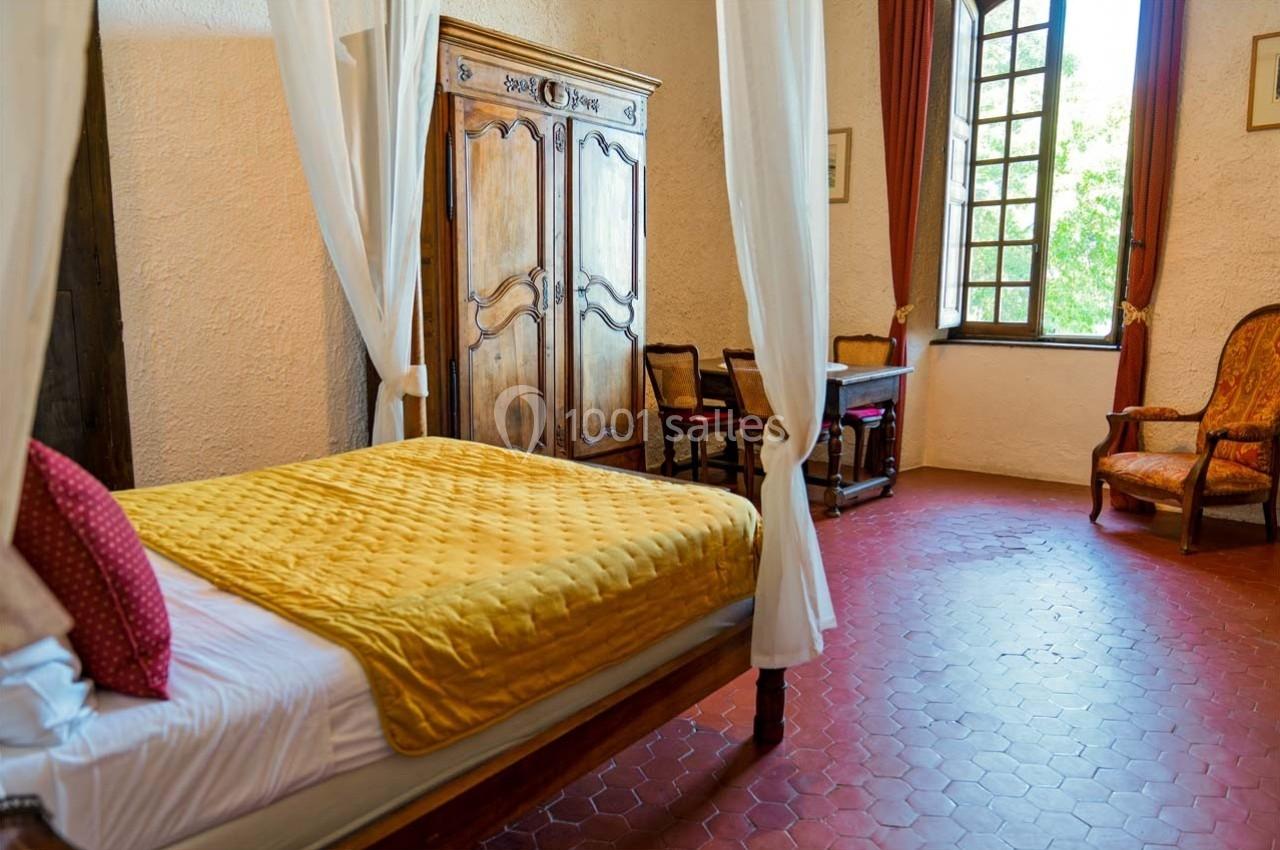 Chambre lumineuse avec lit à baldaquin, armoire en bois, sol en terre cuite et fenêtre donnant sur un jardin.