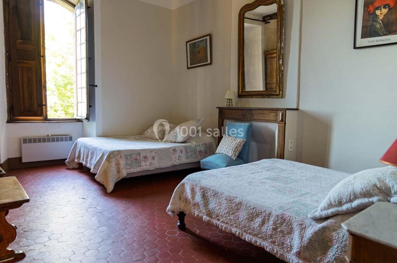 Deux lits simples avec couvre-lits blancs dans une chambre lumineuse au sol en terre cuite, avec une fenêtre ouverte.