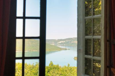 Vue sur un lac entouré de collines verdoyantes à travers une fenêtre ouverte avec des volets en bois.