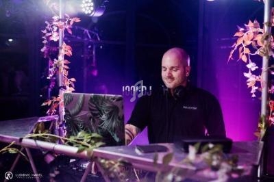 Un DJ mixe sur une scène décorée de plantes, éclairée par des lumières violettes et roses.