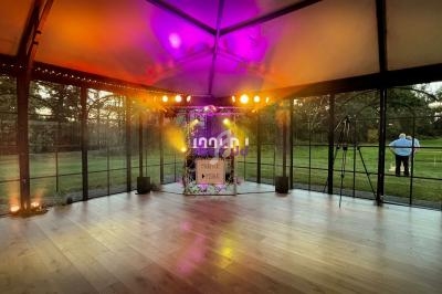 Salle vitrée avec parquet éclairée par des lumières colorées, vue sur un jardin en arrière-plan.