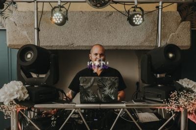 Un DJ souriant derrière une table de mixage, entouré de lumières et d'équipements audio.