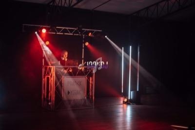 Un DJ mixe sur une scène éclairée par des projecteurs rouges dans une ambiance sombre.