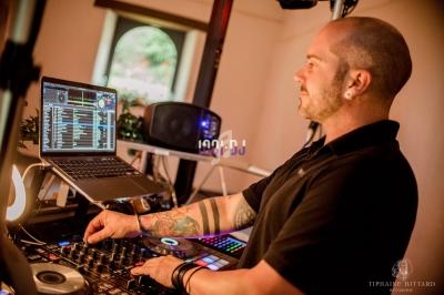 Un DJ mixe de la musique sur une console avec un ordinateur portable dans un environnement intérieur éclairé.