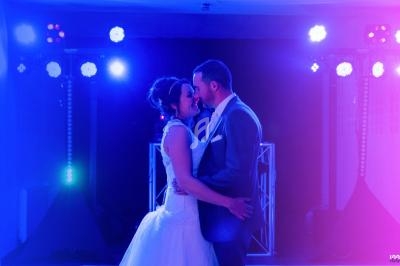 Un couple en tenue de mariage danse sous des lumières colorées dans une salle sombre.