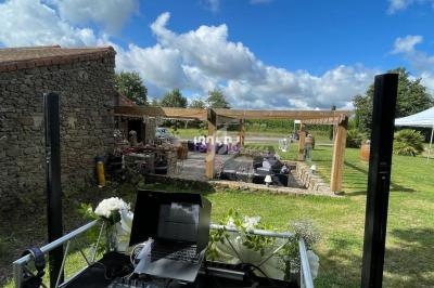 Poste de DJ avec platines et ordinateur, installé en extérieur près d'une grange en pierre et d'une pergola sous un ciel…