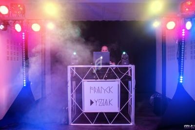 Un DJ mixe sur une scène éclairée par des projecteurs colorés et entourée de fumée.