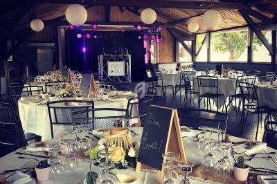 Salle de réception décorée avec des tables dressées, des lanternes suspendues et une scène avec équipement de DJ.