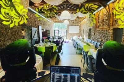 Salle de réception décorée avec des tables dressées, des éclairages colorés et un poste de DJ au premier plan.