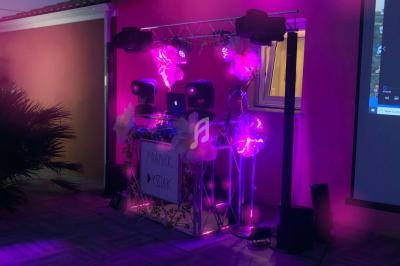 Installation de matériel de DJ avec éclairage violet et décorations lumineuses, en extérieur près d'un mur.