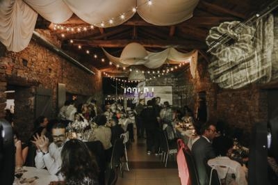Salle en pierre éclairée par des guirlandes lumineuses, avec des invités assis à des tables lors d'un événement festif.