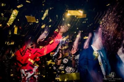 Des personnes dansent sous des confettis dorés dans une ambiance festive et éclairée par des lumières colorées.