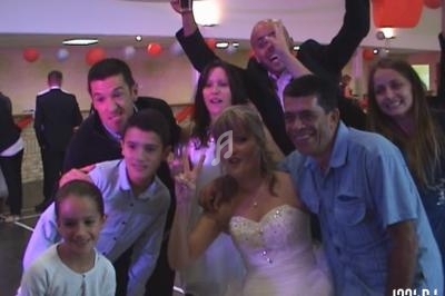 Un groupe de personnes, dont une mariée en robe blanche, pose joyeusement lors d'une célébration en intérieur.