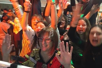 Des personnes souriantes lèvent les bras et posent joyeusement devant un écran dans une ambiance festive en intérieur.