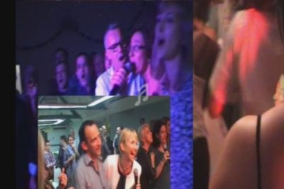 Des personnes chantent et dansent lors d'une fête animée, éclairée par des lumières colorées.