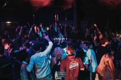 Groupe de personnes dansant dans une ambiance festive avec éclairages colorés dans une salle sombre.