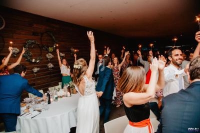 Des invités dansent et lèvent les bras avec des étincelles dans une salle de réception décorée en bois.