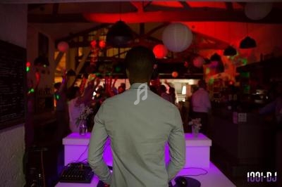 Un DJ de dos anime une soirée dans une salle décorée de lanternes, avec des invités dansant en arrière-plan.