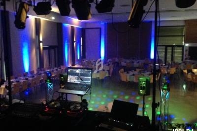 Salle de réception éclairée par des lumières colorées, vue depuis une table de mixage avec ordinateur et platines DJ.