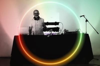 Un DJ mixe de la musique derrière une table équipée de matériel audio, avec un cercle lumineux coloré en surimpression.