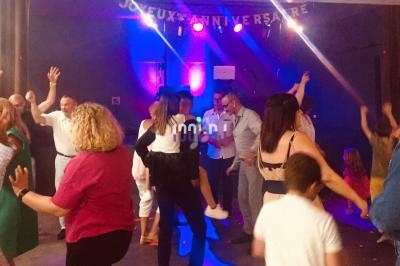 Groupe de personnes dansant dans une salle décorée pour un anniversaire, éclairée par des lumières colorées.