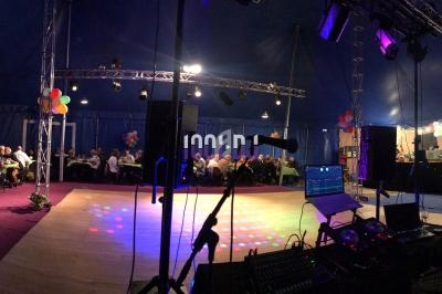 Intérieur d'un chapiteau avec une piste de danse éclairée, des invités assis à des tables et un espace technique visible.