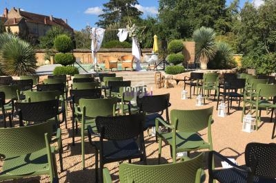 Chaises vertes alignées en extérieur face à une scène décorée avec des tissus suspendus et des plantes.