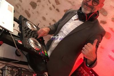 Un homme souriant en costume utilise une table de mixage dans un environnement éclairé en rouge.
