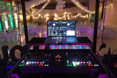 Poste de DJ avec platines et ordinateur allumé, installé dans une salle de réception décorée de guirlandes lumineuses.