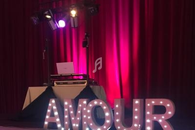 Lettres lumineuses formant le mot ’AMOUR’ devant un rideau rouge et un équipement de DJ éclairé.